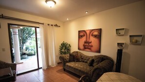 A living room with a sofa, a dining table, and a large painting on the wall. - Anona Guesthouse (Sardinal)