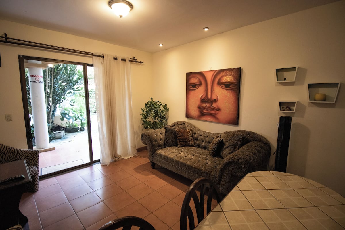 A living room with a sofa, a dining table, and a large painting on the wall.