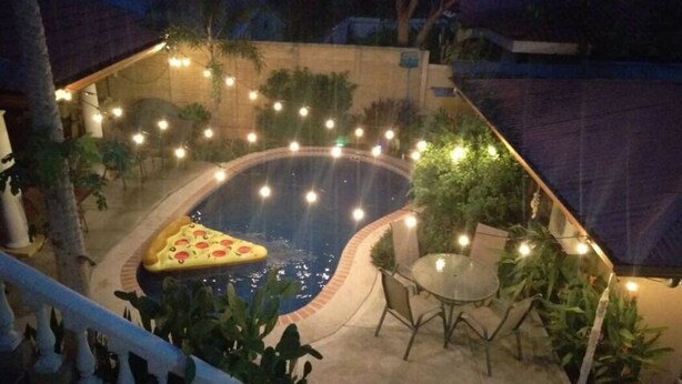 A swimming pool with a pizza float, surrounded by plants and string lights. - Anona Guesthouse (Sardinal)