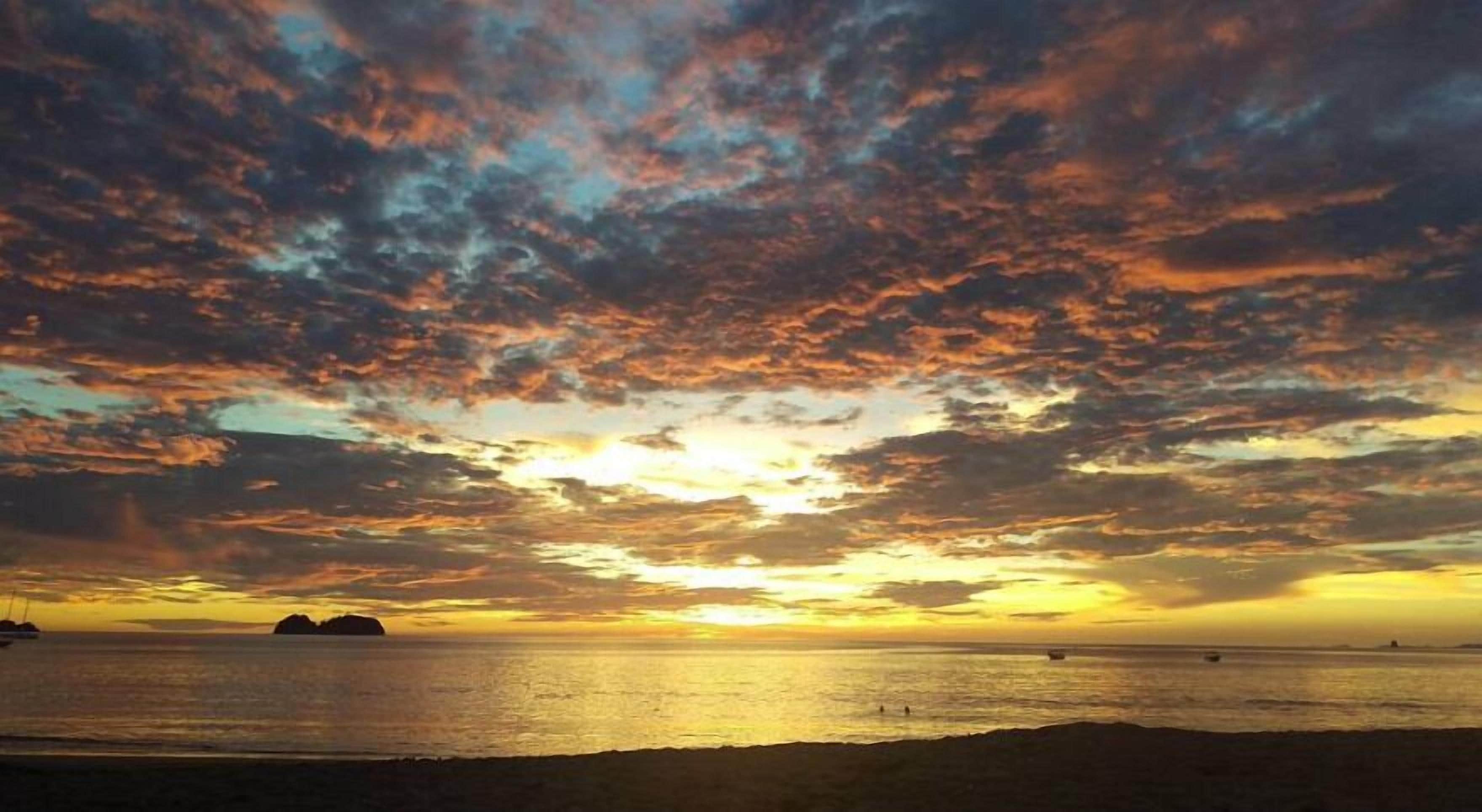 A sunset over a beach with boats and distant landforms.