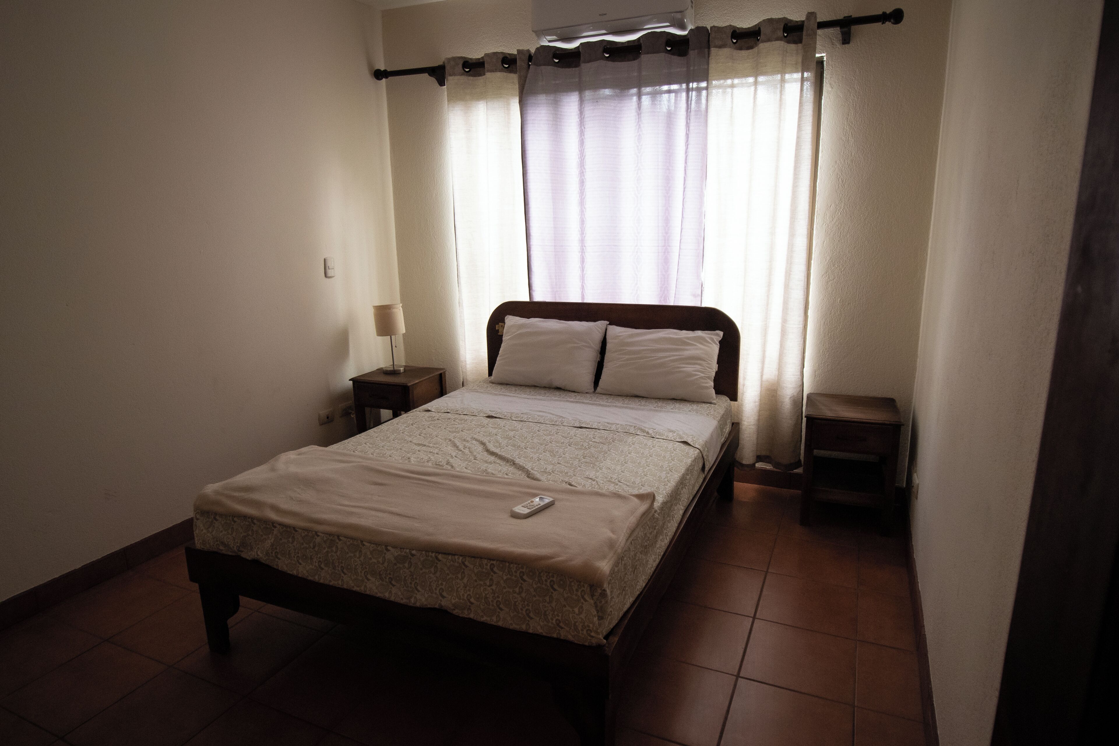 Une chambre à coucher avec un lit, une table de chevet, une commode et une télécommande posée sur le lit.
