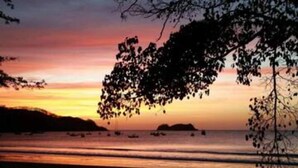 A beach scene with a sunset, calm sea, and boats. - Anona Guesthouse (Sardinal)
