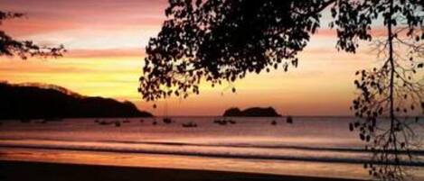 A beach scene with a sunset, calm sea, and boats.