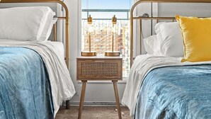Et hotelværelse med to senge, et vindue med udsigt til bygninger og et natbord med en lampe.