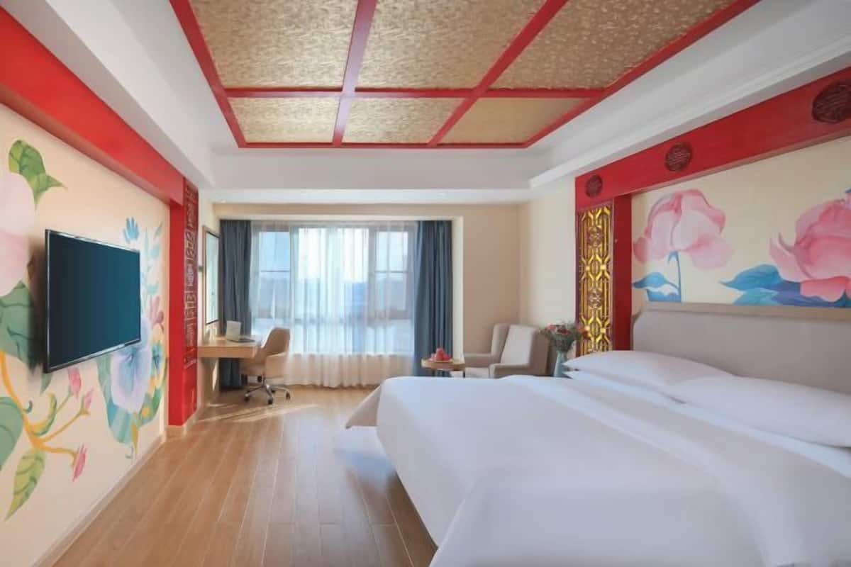 A hotel room with a bed, a desk, a chair, a TV, and a window with curtains.