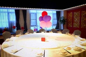 Une table ronde dressée pour un repas, agrémentée d’un centre de table rouge, et entourée de chaises et de tables à manger.