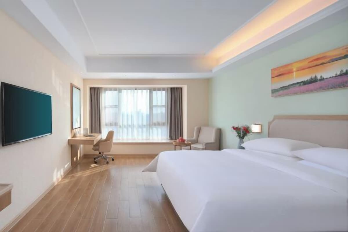 Een hotelkamer met een groot bed, een bureau, een stoel, een televisie en een schilderij aan de muur.