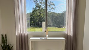 Une pièce avec une console blanche, une plante en pot et une vue sur un paysage verdoyant par la fenêtre.
