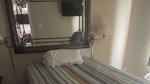Ein Schlafzimmer mit einem Bett, einem Spiegel, einer Lampe und einer Tür.