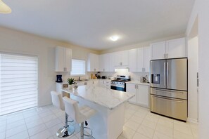 A modern kitchen with white cabinets, a marble island, stainless steel appliances, and a bar stool.