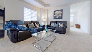 Ein modernes Wohnzimmer mit zwei Ledersofas, einem Glastisch und einem großen floralen Gemälde an der Wand.