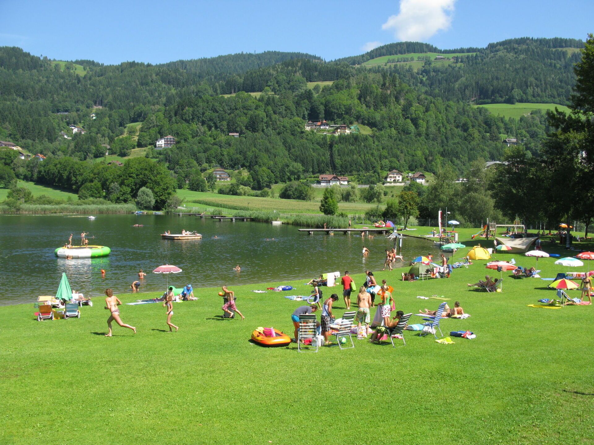 Un parc au bord du lac, avec des pelouses, des bateaux et des parasols.