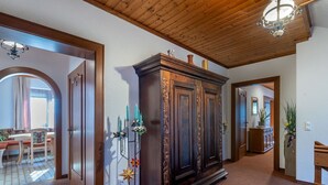 Un couloir avec un plafond en bois, une grande armoire sombre en bois ornée de sculptures complexes, et un motif décoratif en forme d’étoile sur le sol.