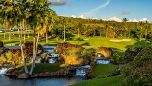 Un campo de golf con una cascada, palmeras y cielo despejado.