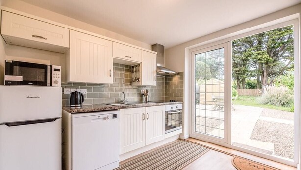 A modern kitchen with white cabinetry, a built-in microwave, a coffee maker, and a large window offering a view of the outdoors. - Harbour View, Walberswick (Walberswick)