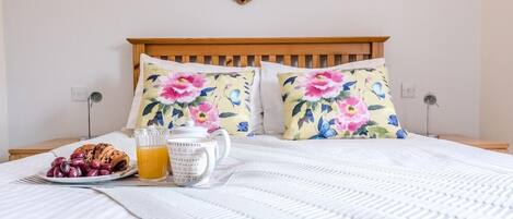 Uma cama bem arrumada com almofadas florais, um prato de uvas, um croissant e um copo de suco de laranja.