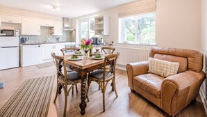 A spacious kitchen with white cabinets, a dining table set for four, and a leather sofa in the living area. - Harbour View, Walberswick (Walberswick)