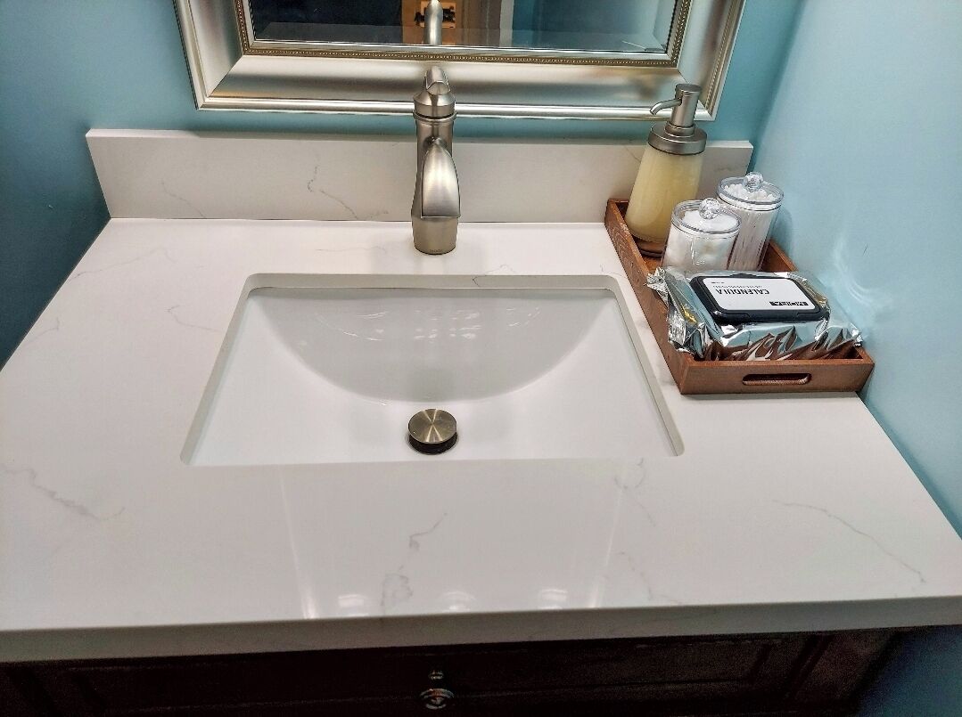 Une salle de bain avec un lavabo en marbre blanc, un robinet argenté, un miroir avec un cadre doré et des articles de toilette disposés dans un plateau en bois.