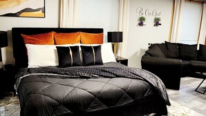 Une chambre moderne avec un grand lit, un canapé noir et un mur décoratif orné d’une inscription : « Soyez les bienvenus ».