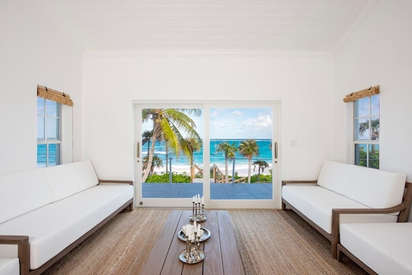 A room with a view of the beach, white sofas, a wooden coffee table, and a door with glass panels. - C Breeze 4 Bedroom Home (Double Bay)