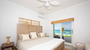 Un dormitorio con una cama grande, cabecera de madera, vista al océano y ventilador de techo.
