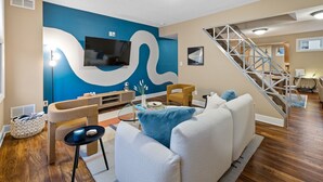Una sala moderna con un televisor grande, una escalera y una pared de acento azul.