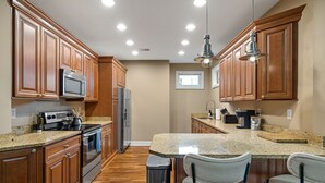 Una cocina con gabinetes de madera, encimeras de granito, electrodomésticos de acero inoxidable y una zona de bar con dos sillas.