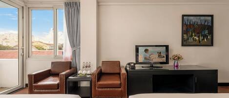 A hotel room with two beds, a desk with a television, a chair, a window with curtains, and a painting on the wall.