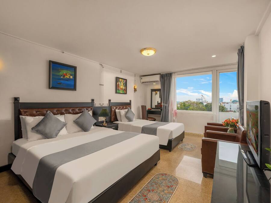 Ett hotellrum med två sängar, ett skrivbord, en tv och ett stort fönster med utsikt över staden.