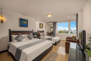Habitación de hotel con dos camas, un escritorio, un televisor y un ventanal con vistas a la ciudad.