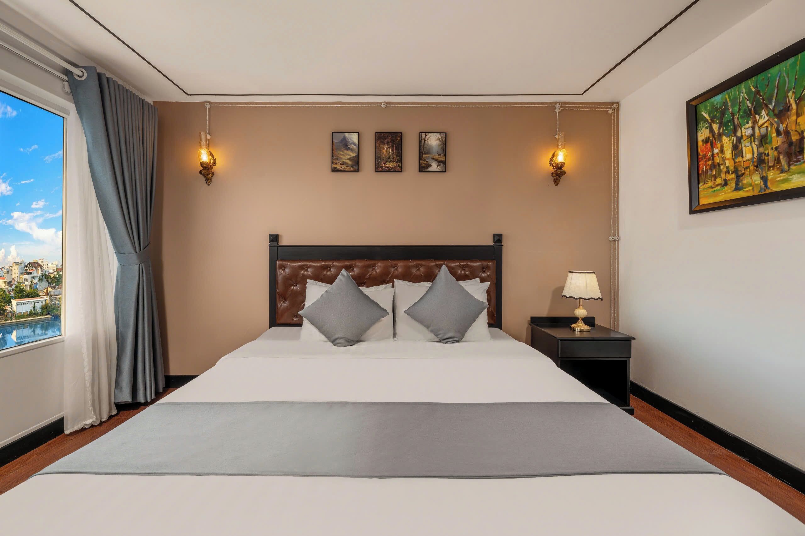 Una habitación de hotel con una cama grande, una mesita de noche con una lámpara y un cuadro en la pared.