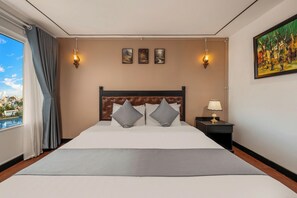 A hotel room with a large bed, a nightstand with a lamp, and a painting on the wall. - Vina Spa Hotel (Hue)