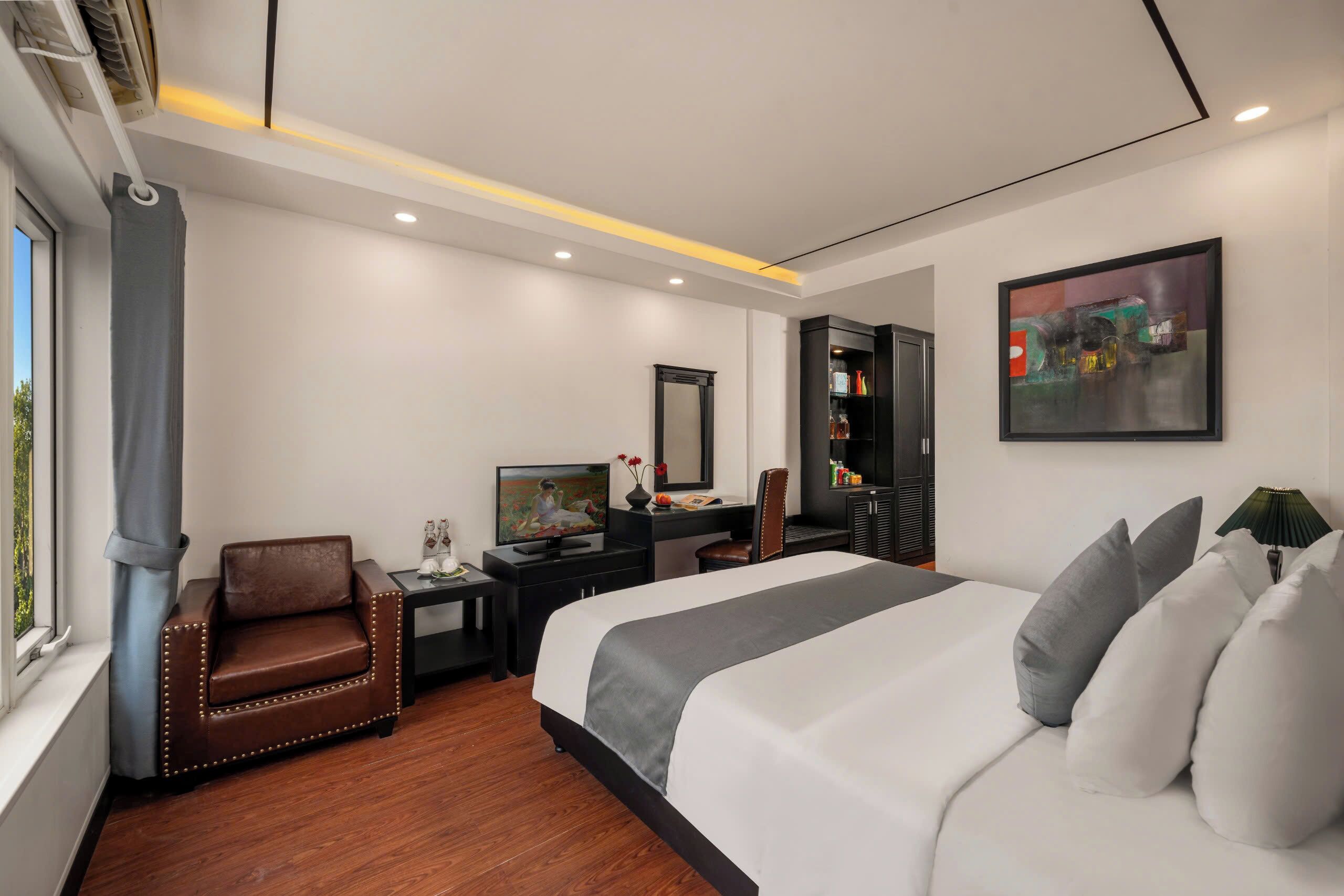 Habitación de hotel moderna con una cama grande, un escritorio con computadora, una silla, un televisor, un armario y un cuadro en la pared.