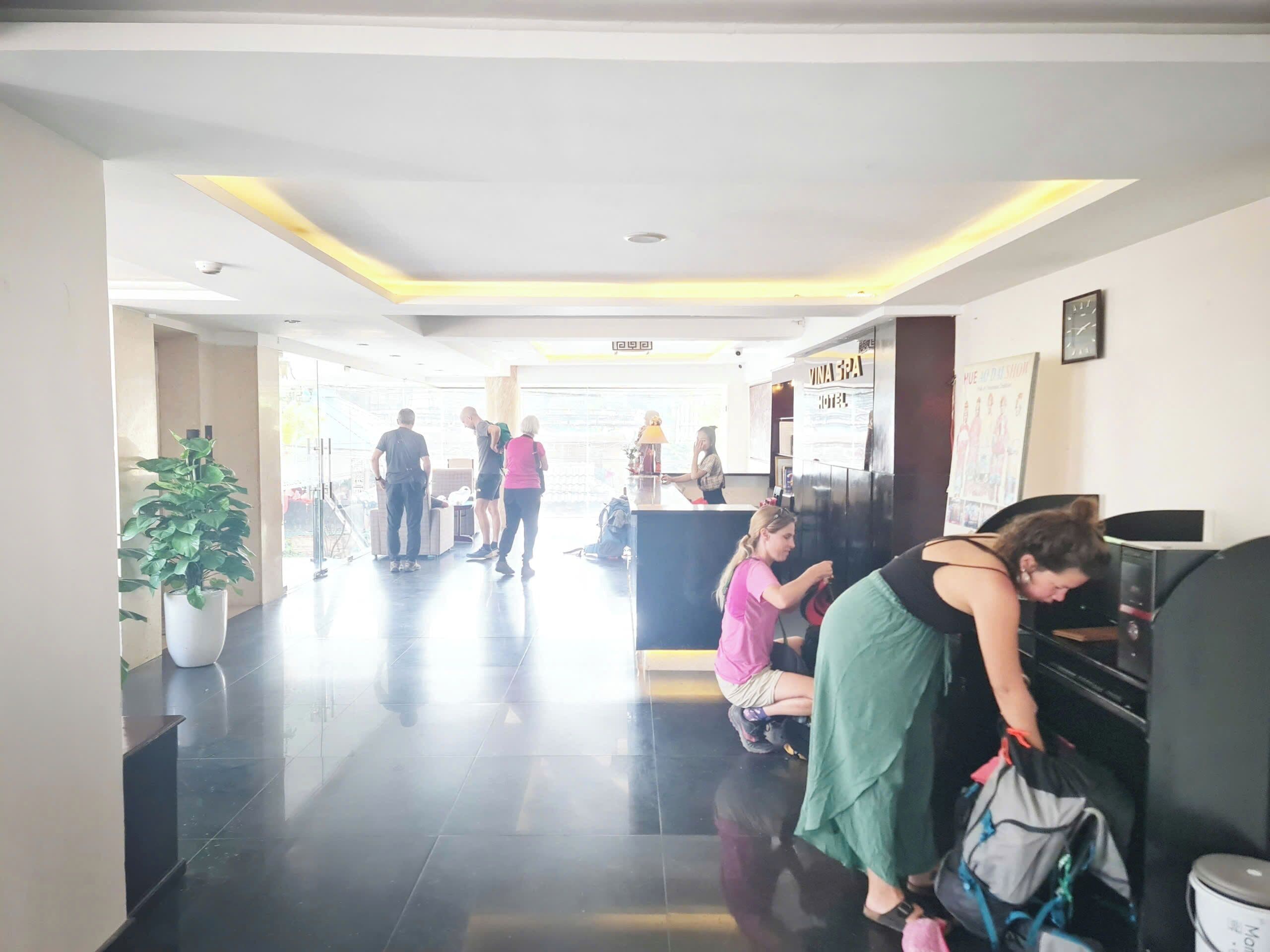 Een hotellobby met een receptiebalie, een plant in pot en een betegelde vloer.
