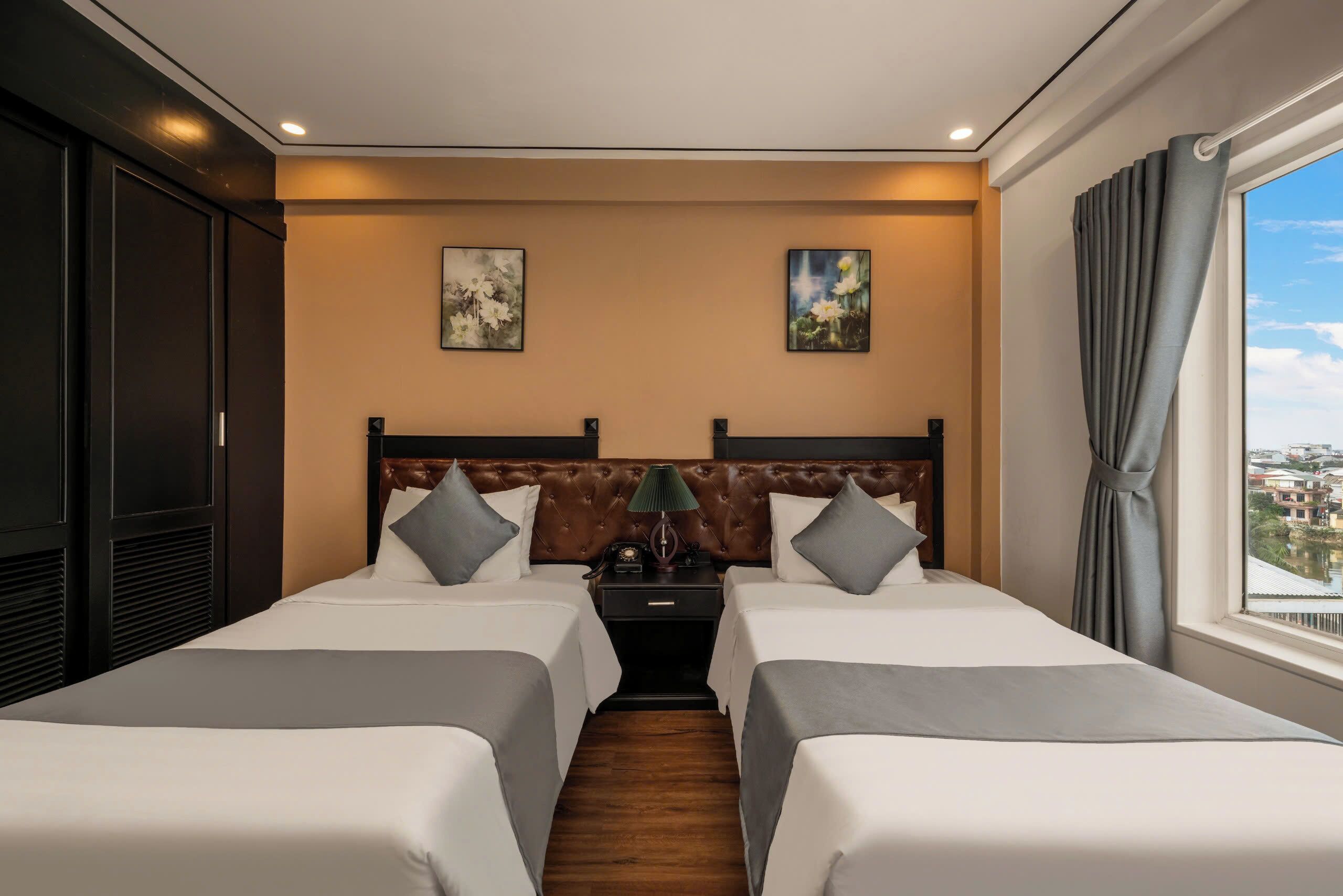 A hotel room with two beds, a large window with curtains, and artwork on the walls.