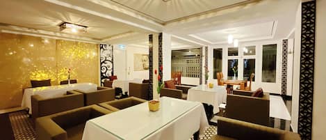 A restaurant with a modern interior, featuring a central dining table surrounded by sofas and chairs, a patterned floor, and decorative wall panels.