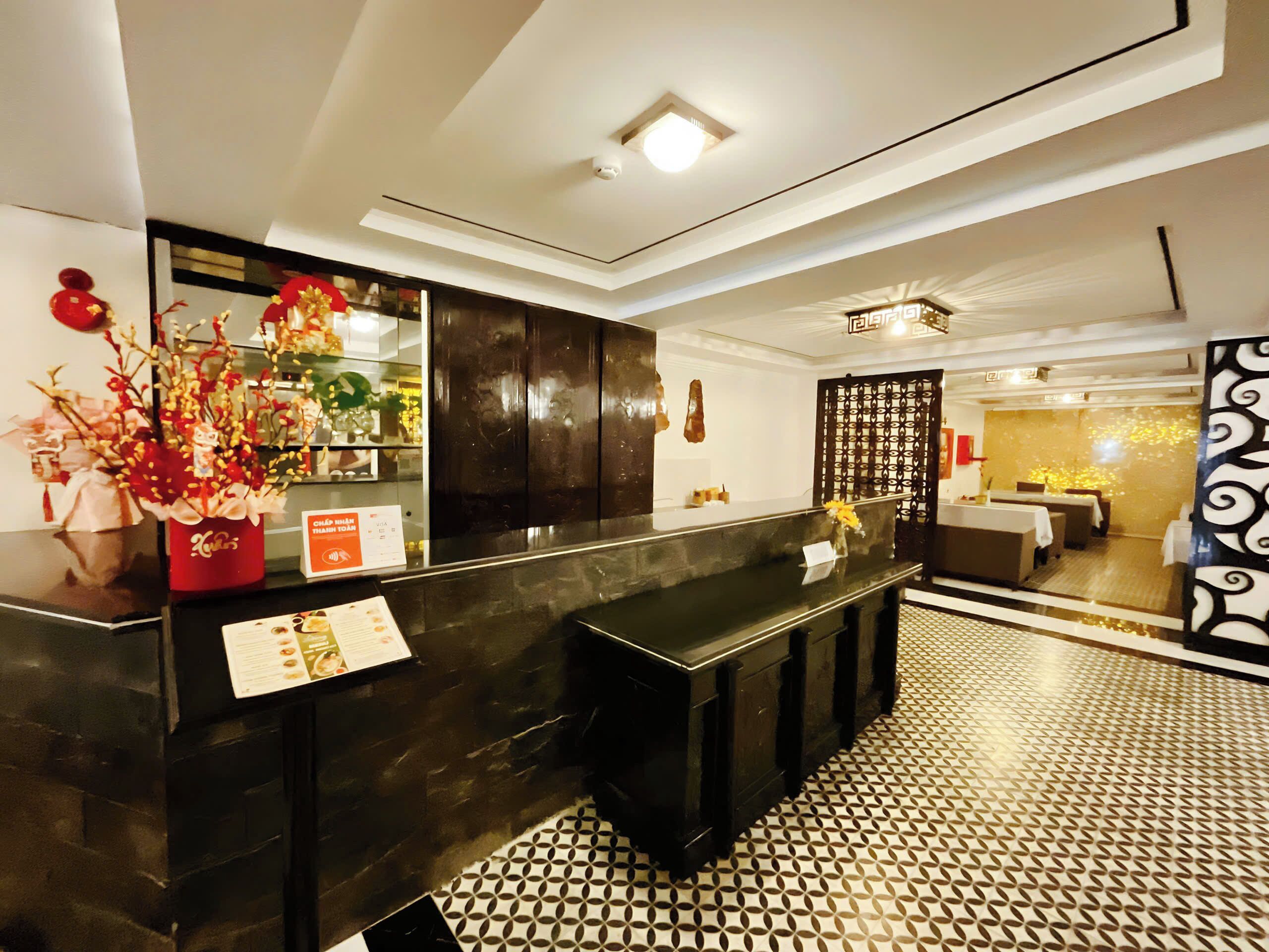 A hotel reception area with a black reception desk, a decorative plant, and a patterned floor.
