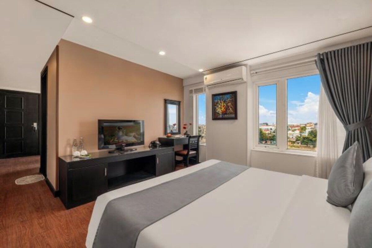 A hotel room with a bed, a TV, a desk, and a window with curtains.