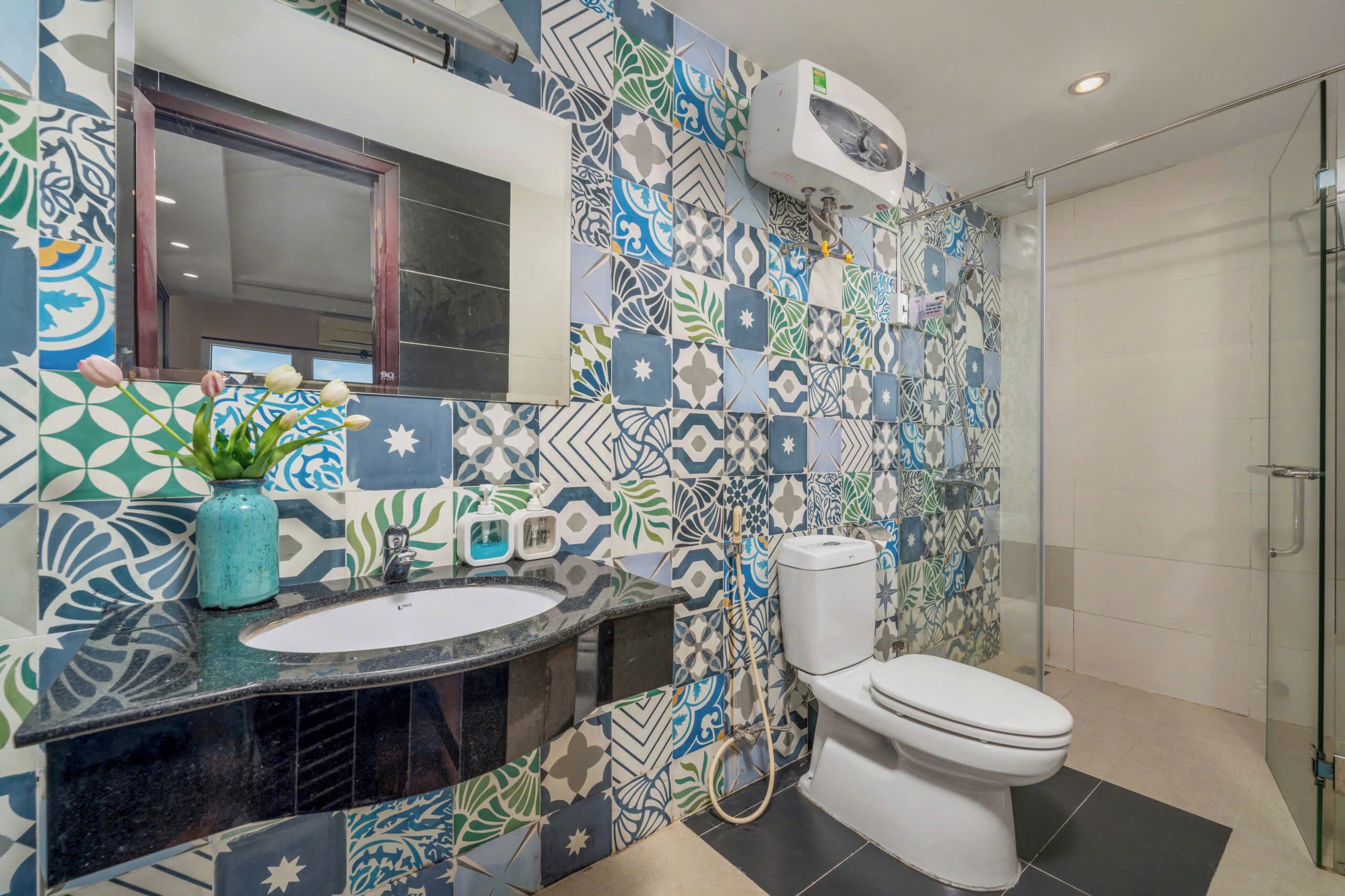 A bathroom with a patterned tile wall, a sink with a mirror, a toilet, and a shower area.