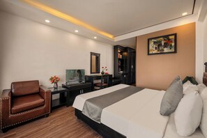 A hotel room with a large bed, a desk with a computer, a chair, a bookshelf, and a painting on the wall. - Vina Spa Hotel (Hue)