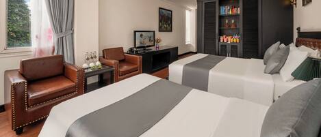 A hotel room with two beds, a desk, a chair, a television, and a bookshelf.