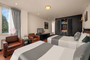 Ett hotellrum med två sängar, ett skrivbord, en stol, en tv och en bokhylla.
