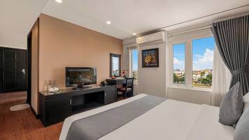 A hotel room with a bed, a desk, a television, and a window with a city view.