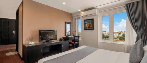 A hotel room with a bed, a desk, a television, and a window with a city view.