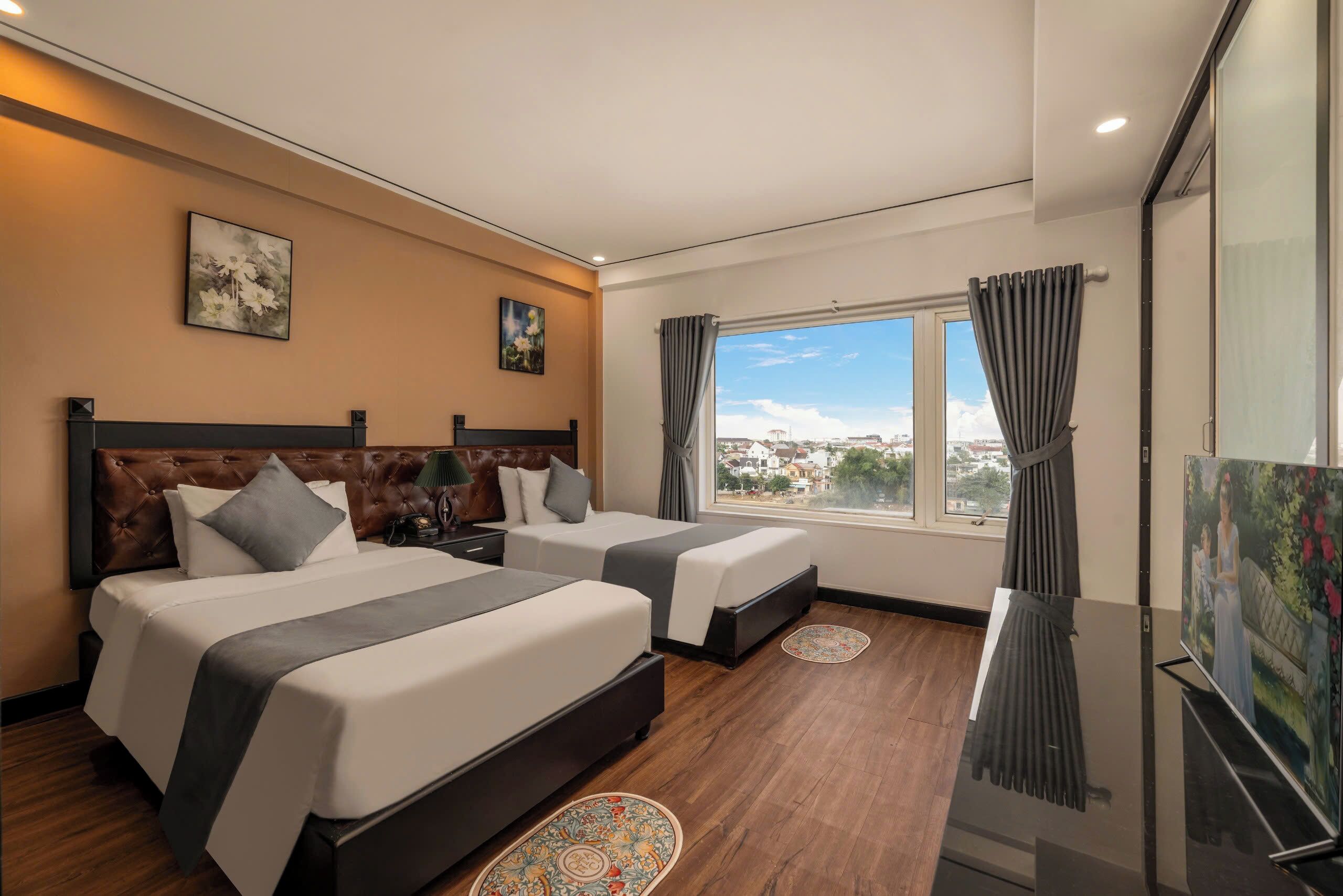 Camera d'albergo con due letti, un'ampia finestra con tende e un quadro appeso al muro, con vista sulla città.