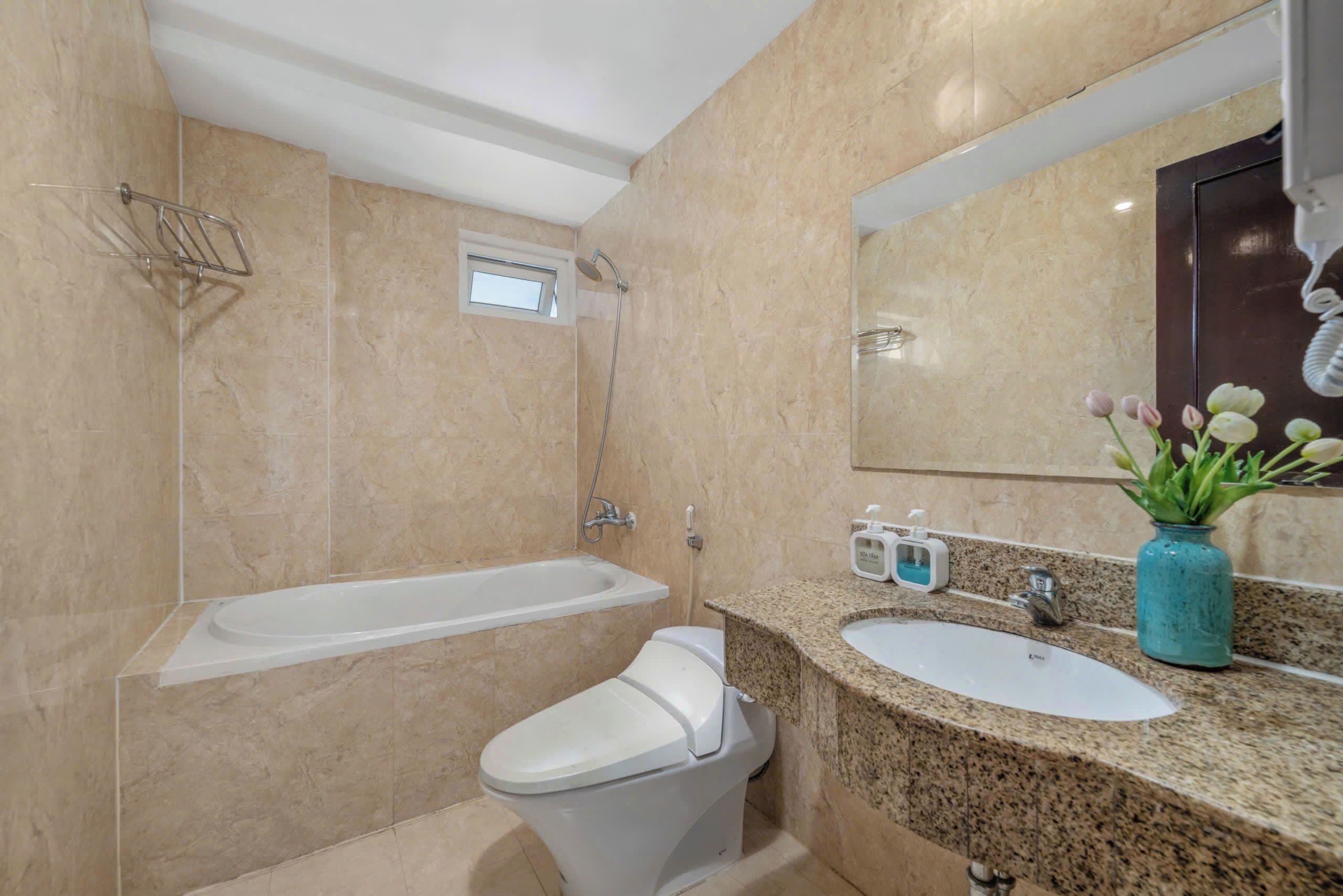 Un baño con bañera, inodoro, lavamanos y un espejo con una planta.