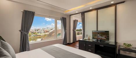 A modern hotel room with a large bed, a flat-screen TV, a desk, and a view of a cityscape through the window.