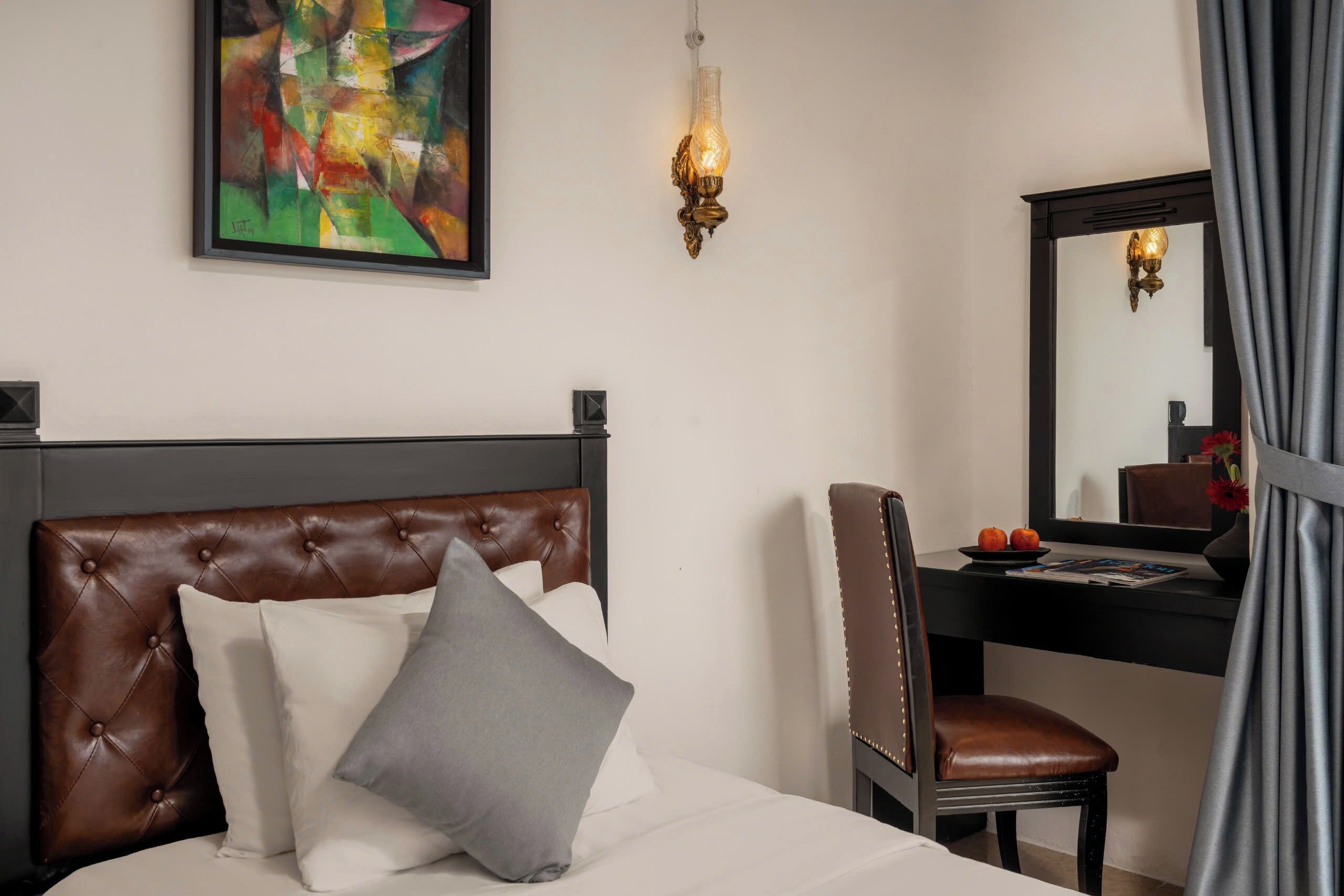 A hotel room with a bed, a chair, a desk, a mirror, and a painting on the wall.
