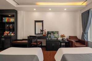 A hotel room with two beds, a desk with a chair, a bookshelf, a television, and a window with curtains. - Vina Spa Hotel (Hue)