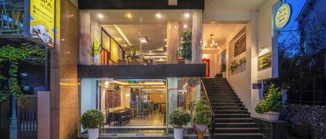 A hotel entrance with a staircase leading to the upper floor, glass doors, and potted plants.